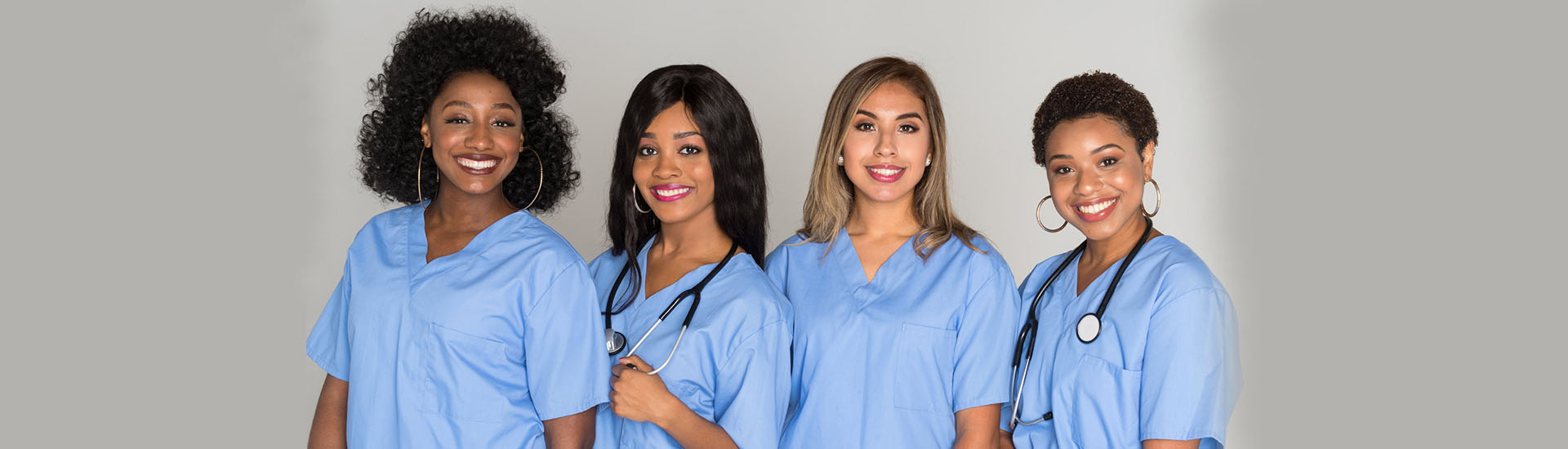 Four smiling nurses in blue scrubs.