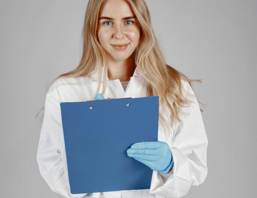 Woman in lab coat holding clipboard.
